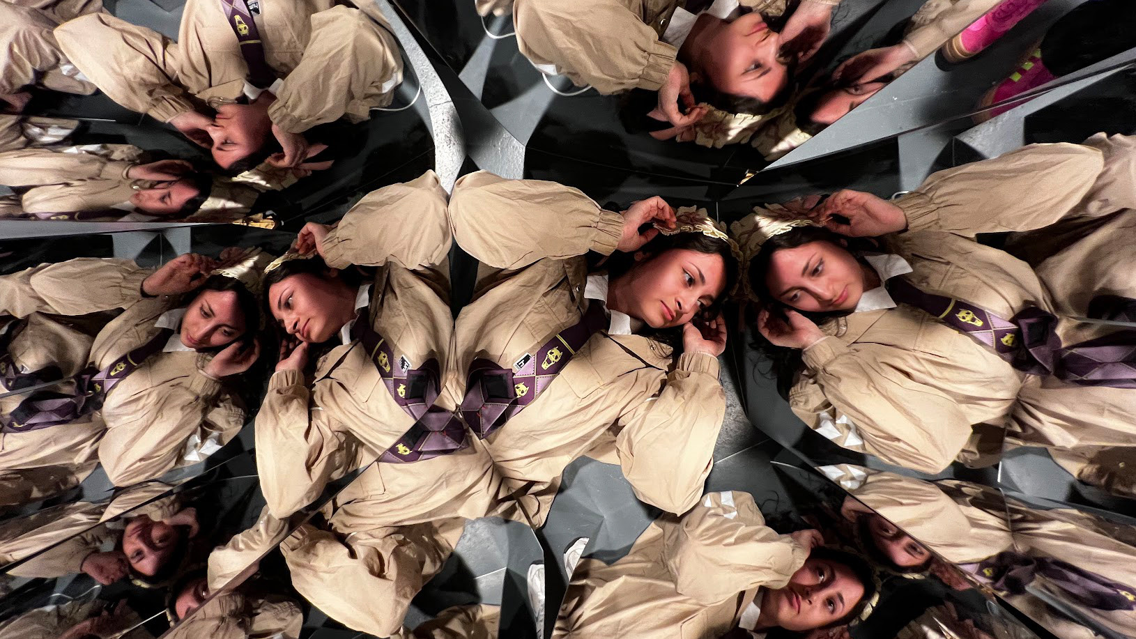 Eine Person liegt auf dem Boden und schaut in zahlreiche Spiegel, die ihr Spiegelbild vervielfachen