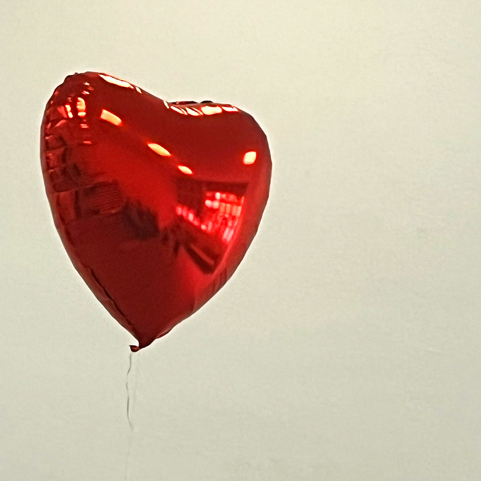 roter Herzluftballon schwebt vor einer weißen Wand