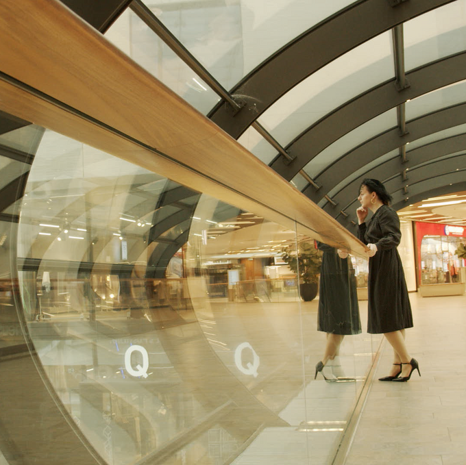Person im schwatzen Kleid steht in einem gläsernen Tunnel