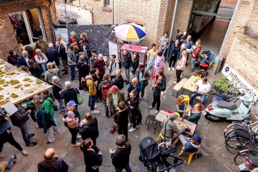 Foto auf einen Hinterhof von oben. Viele Menschen stehen mit Sektgläsern im Hof und unterhalten sich. Die Stimmung ist ausgelassen