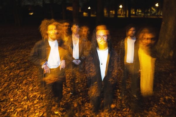 SCP - 055 Foto von vier Männern auf einem Boden voller Herbstblätter. Das Bild ist verschwommen, der Farbton ein warmes gelb.