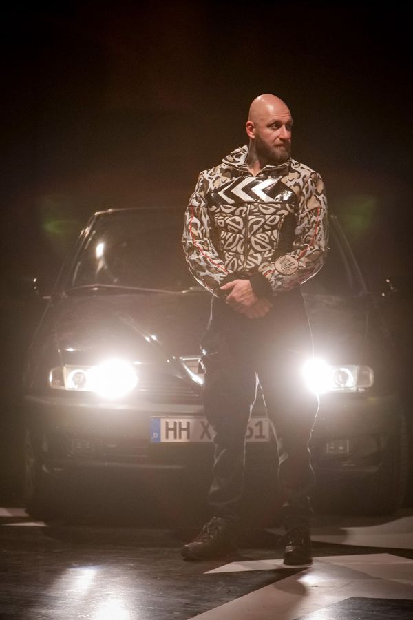 Security Mann steht breitbeinig in der Dunkelheit vor einem Auto dessen Scheinwerfer ihn von hinten anstrahlen