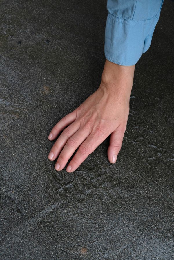hear me see Eine Hand betastet einen Fußabdruck auf einem anthrazitfarbenen Boden