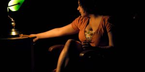 Frau sitzt in der Dunkelheit und schaltet eine Schreibtischlampe mit einem grünen Lampenschirm an
